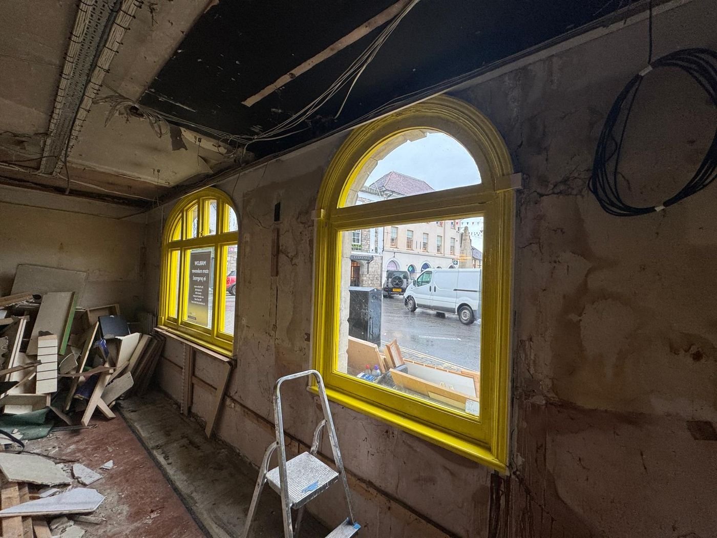 Shop interior before work: stripped walls, exposed ceiling and yellow arched windows